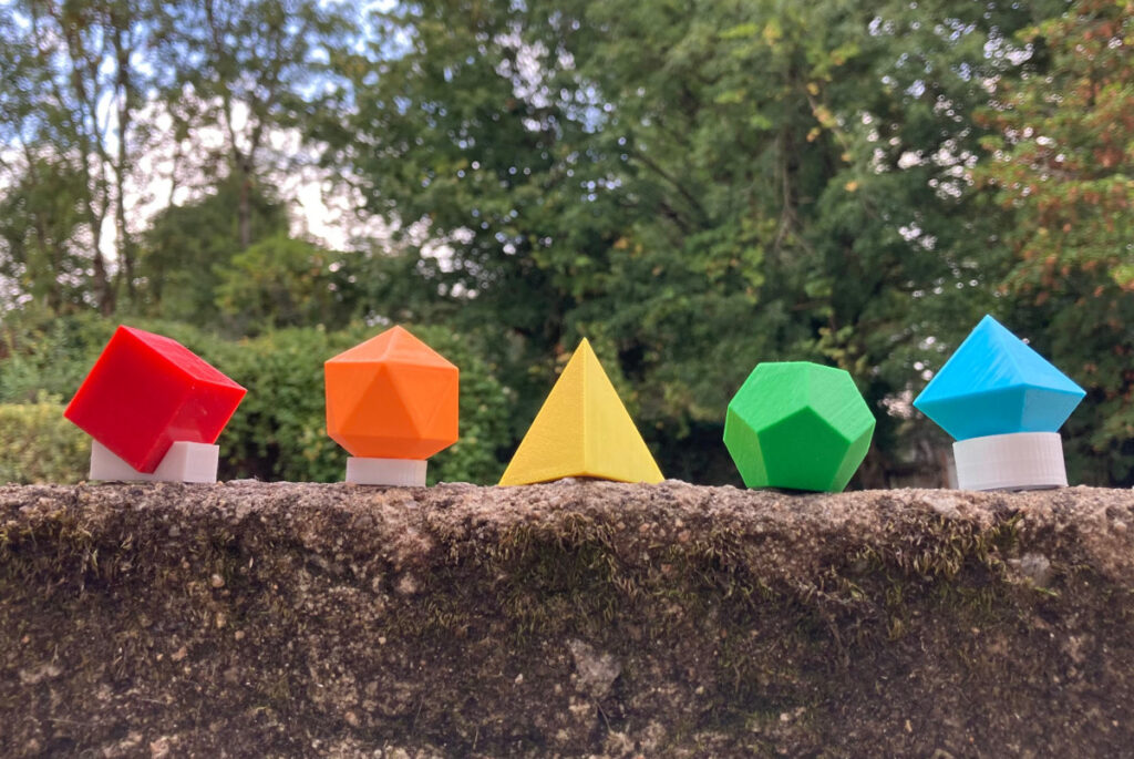 Les 5 Solides de Platon en couleurs fabriqués par Isoris sur un muret avec des arbres en arrière plan